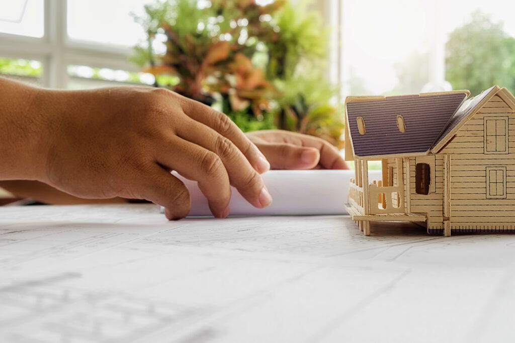 Ręce inżyniera przy planach i miniaturze domu