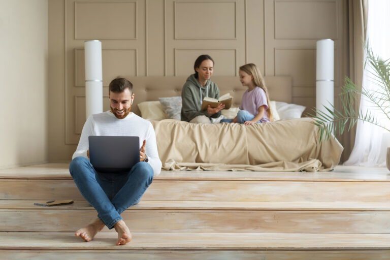 Mężczyzna przed laptopem, w tle mieszkanie i jego rodzina
